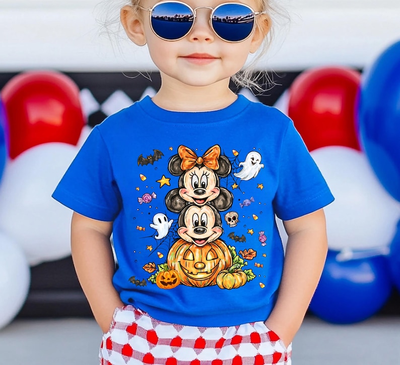 Puede incluir: Una camiseta azul de manga corta con un dise&ntilde;o de Halloween. El gr&aacute;fico incluye a Minnie y Mickey Mouse apilados encima de una calabaza tallada, rodeados de fantasmas, murci&eacute;lagos y caramelos. Llevada por un ni&ntilde;o.
