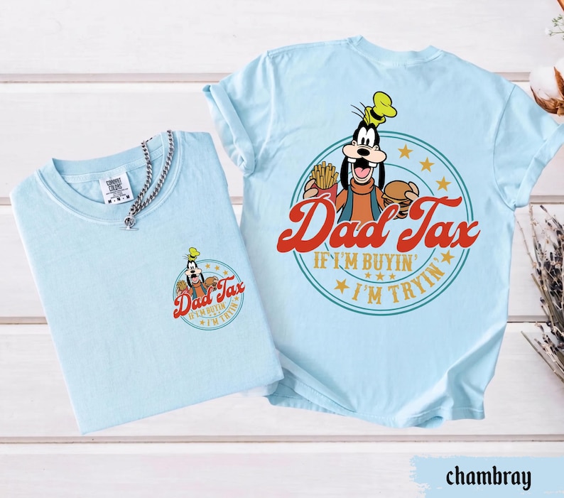 May include: Two light blue t-shirts. One shirt has a small graphic of Goofy with the words "Dad Tax" and "If I'm buyin' I'm tryin'". The other shirt has a larger version of the same graphic on the back.