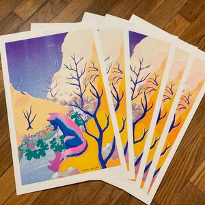 May include: A stack of art prints featuring a colorful illustration of a fox-like creature with blue and pink fur, set against a landscape with yellow, purple, and orange hues. Bare trees and a mountain range are also visible.