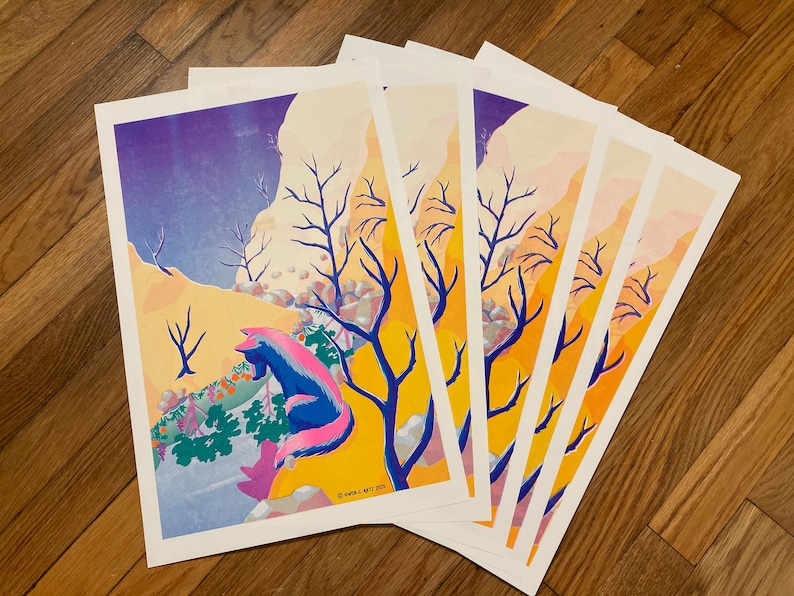May include: A stack of art prints featuring a colorful illustration of a fox-like creature with blue and pink fur, set against a landscape with yellow, purple, and orange hues. Bare trees and a mountain range are also visible.