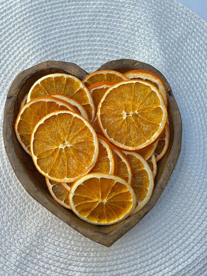 Peut inclure: Un bol en bois en forme de c&oelig;ur rempli de tranches d'orange s&eacute;ch&eacute;es. Les tranches d'orange sont dispos&eacute;es en cercle et sont d'une couleur orange vibrante.