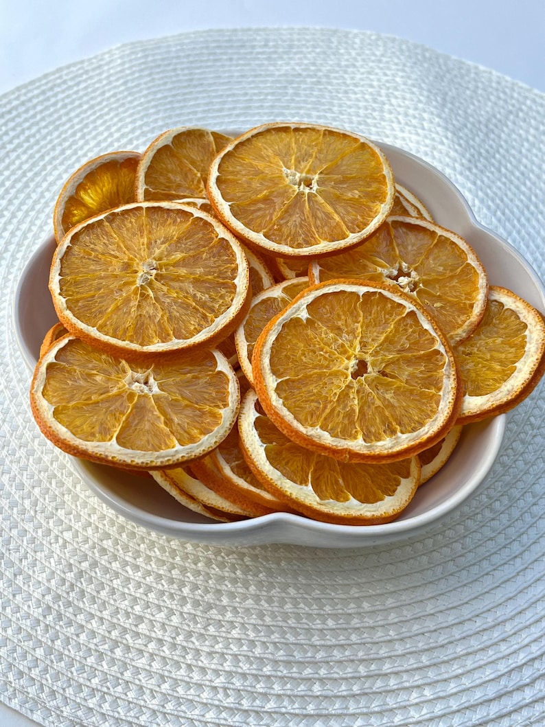 Peut inclure: Un bol blanc rempli de tranches d'orange s&eacute;ch&eacute;es. Les tranches d'orange sont dispos&eacute;es en cercle et sont d'une couleur orange vive.