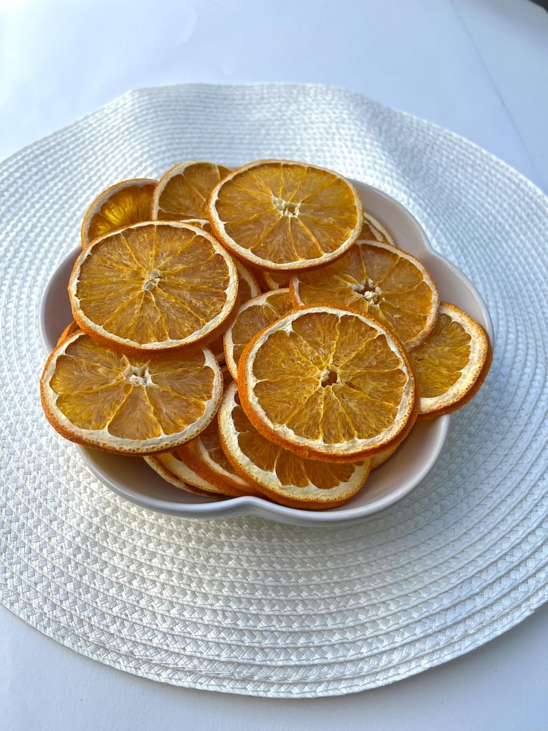 Peut inclure: Un bol blanc rempli de tranches d'orange s&eacute;ch&eacute;es. Les tranches d'orange sont dispos&eacute;es en cercle et sont d'une couleur orange vive.