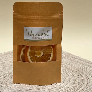 Peut inclure: Un sac en papier brun avec une fen&ecirc;tre transparente montrant des tranches d'orange s&eacute;ch&eacute;es. Le sac porte une &eacute;tiquette qui dit "Harvest Harmony."