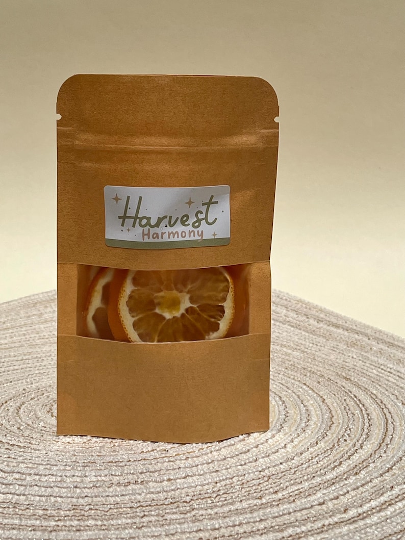 Peut inclure: Un sac en papier brun avec une fen&ecirc;tre transparente montrant des tranches d'orange s&eacute;ch&eacute;es. Le sac porte une &eacute;tiquette qui dit "Harvest Harmony."
