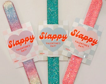 May include: Three glitter-covered nail files with Valentine's Day cards attached. The cards are pink and white with a red heart and the text "Slappy Valentine's Day!" The nail files are pink, blue, and green.