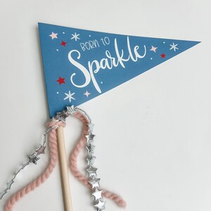 Könnte beinhalten: Ein blaues Wimpel mit weißen Sternen und dem Text "Born to Sparkle" auf weißem Hintergrund. Eine rosa und silberne Sternen-Girlande ist an dem Wimpel befestigt.