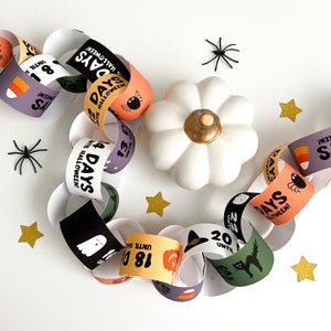 Puede incluir: Una cadena de cuenta atrás de Halloween con eslabones de papel de colores que presentan diferentes ilustraciones con temática de Halloween y el número de días hasta Halloween. La cadena está decorada con pequeñas estrellas doradas y arañas negras.