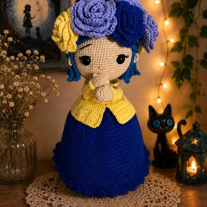 Peut inclure: Une poupée en crochet faite à la main avec des cheveux bleus, de grands yeux noirs et une couronne de roses en laine jaune, violet clair et bleu foncé. La poupée porte un gilet jaune sur une jupe bleu foncé, les mains jointes près du visage.