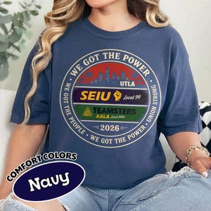 May include: Navy blue t-shirt with a circular graphic that reads "WE GOT THE POWER." The graphic includes the text "UTLA," "SEIU Local 99," "TEAMSTERS AALA Local 2010," and "2026." The shirt also has the words "COMFORT COLORS" and "Navy" on it.