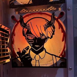 Puede incluir: Una obra de arte retroiluminada y en capas que representa a un personaje de anime estilizado con cuernos y cabello negros. El personaje está silueteado contra un resplandor anaranjado, con detalles rojos que parecen gotas de sangre. La obra está montada sobre una superficie clara.