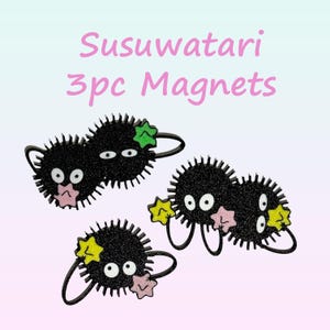 May include: Three black Susuwatari magnets with white eyes, pink mouths, and star-shaped accents in green and yellow. The magnets have a glittery texture and are arranged on a gradient background. Text reads "Susuwatari 3pc Magnets".