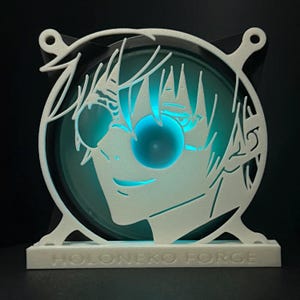 Puede incluir: Un ventilador blanco impreso en 3D con un recorte del rostro de un personaje. El personaje tiene el pelo negro corto, lleva gafas de sol y sonríe. El ventilador está iluminado desde atrás con una luz azul. La base del ventilador tiene el texto "HOLONEKO FORGE" impreso en ella.