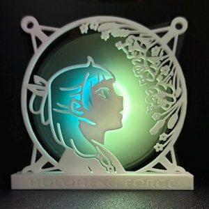 May include: A white 3D printed lamp featuring a cut-out design of a girl's profile and flowers. The lamp is illuminated from behind, creating a green and blue glow. The base of the lamp displays the text "HOLO-NO FORCE".