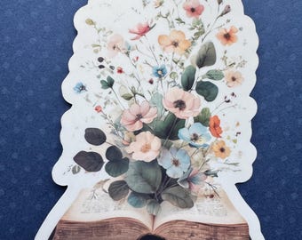 May include: A die-cut sticker featuring an open book with a bouquet of colorful flowers. The flowers include pink, orange, blue, and white blooms with green leaves. The book has aged, brown pages and is set against a blue background.