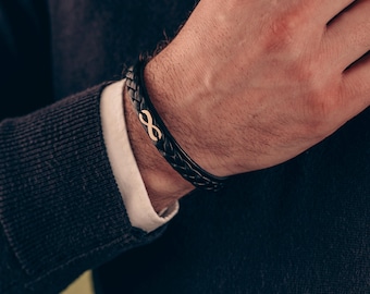 May include: A black leather bracelet with a gold infinity symbol charm.