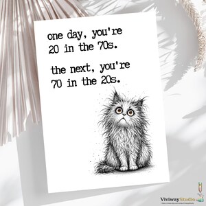May include: A white greeting card featuring a black ink illustration of a fluffy, wide-eyed cat. The text reads: one day, you're 20 in the 70s. the next, you're 70 in the 20s. The design is centered on the card with a clean, minimalist aesthetic.