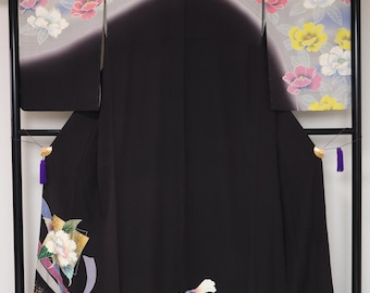 May include: A black kimono with floral and ribbon designs. The top portion features a gradient of gray to black with yellow, pink, and white flowers. The bottom has a gold, white, and blue ribbon design with a large white flower.
