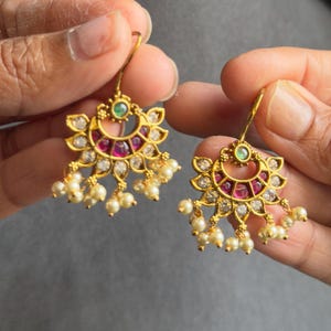 Può includere: Orecchini dorati con un design floreale, con pietre preziose rosse e trasparenti e piccole perle bianche. Gli orecchini hanno una chiusura a gancio.