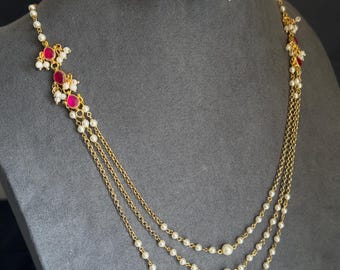 May include: A gold-tone multi-strand necklace featuring three delicate chains accented with small white pearls and teardrop-shaped pink stones, paired with matching drop earrings that feature similar pink stones and pearl clusters.