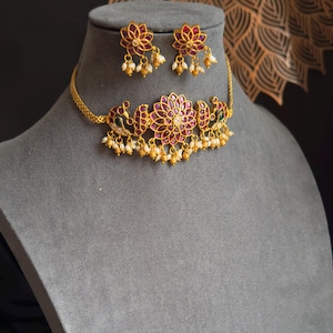 May include: A gold choker necklace with a red flower design and pearl accents. Matching earrings with a red flower design and pearl accents.