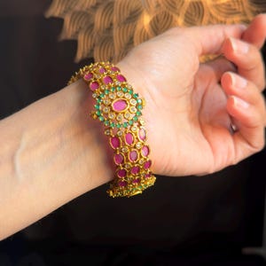 May include: Gold bangle bracelet with pink and green gemstones. The bracelet is made of multiple bands with a floral design.