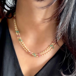 May include: A gold chain necklace with pink and green gemstones. The necklace is layered and has a delicate design.