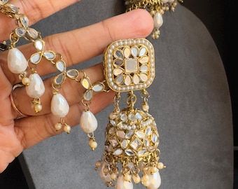 May include: A pair of gold-tone earrings with white pearl accents. The earrings feature a square-shaped design with a mirrored center and a dangling bell-shaped charm.