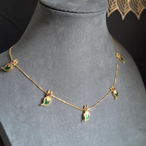May include: A gold necklace with leaf-shaped pendants. Each pendant has a green centre stone and a small red stone. The necklace is displayed on a grey mannequin.