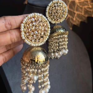May include: Gold tone earrings with a round, clear stone design and a dangling pearl and gold chain fringe.