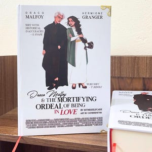 Könnte beinhalten: Ein Buch mit dem Titel "Draco Malfoy & The Mortifying Ordeal of Being in Love" zeigt Illustrationen von Draco Malfoy und Hermine Granger. Das Cover enthält Text und Zitate, mit einem roten Lesebändchen. Das Buch steht auf einem Holzregal.