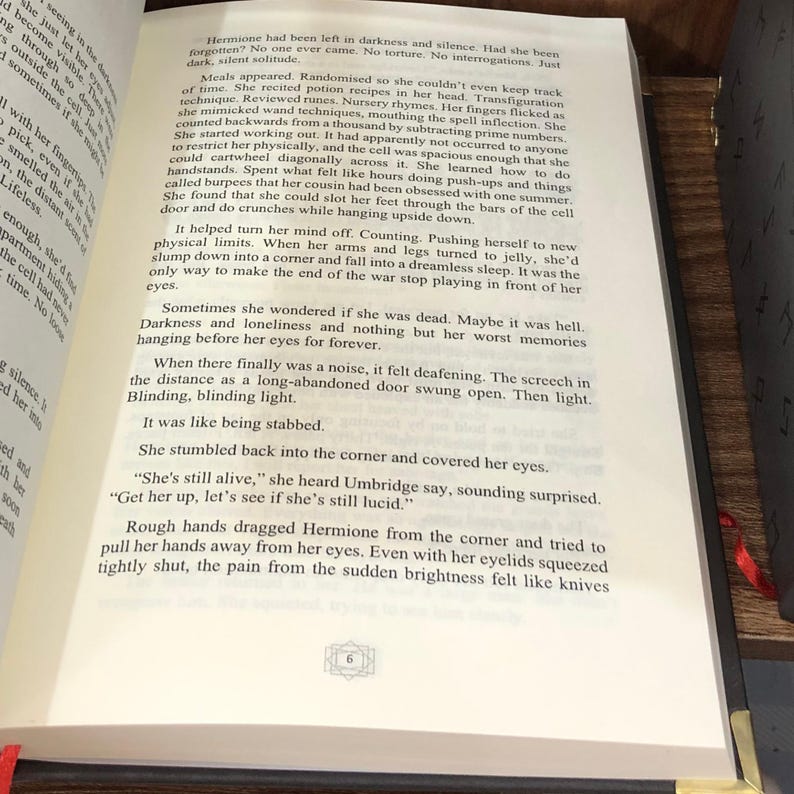 May include: Open book with text on the pages. The text is in English and describes a scene with the character Hermione. The book has a dark brown cover and a red ribbon bookmark.