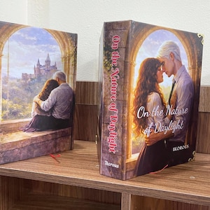 May include: Two hardcover books with the title "On the Nature of Daylight." One book features a couple embracing, the other shows a couple kissing. The spines display the title vertically. The author's name, "Ikorous," is visible on one book.