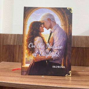 May include: A hardcover book titled "On the Nature of Daylight" with a romantic illustration of a couple embracing. The book cover features a warm color palette with gold corner accents and the author's name, IKOROUS, at the bottom.