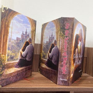 May include: Two decorative bookends featuring a romantic scene of a couple embracing, with a castle in the background. The bookends are titled "On the Nature of Daylight" and have gold-colored corner accents.