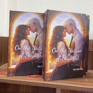 May include: Two hardcover books titled "On the Nature of Daylight" are displayed. The covers feature a romantic illustration of a couple embracing, set against an arched window backdrop. The author's name, Ikorous, is visible.