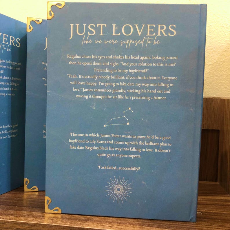 Pu&ograve; includere: Diversi libri con copertine blu e angoli dorati. Il titolo "JUST LOVERS" &egrave; visibile, insieme a estratti dalla sinossi del libro. Il design include una costellazione e un motivo a raggiera.