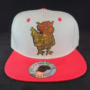May include: A gray and red baseball cap with a patch of a cartoon chicken with a furry head. The patch is yellow, orange, and black. The cap has a sticker on the side that says "Original Snapbacks".