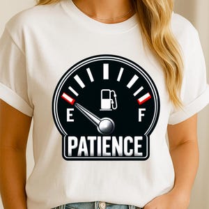 May include: White t-shirt featuring a black gauge design with a fuel pump icon and the word "PATIENCE" in a white rectangle. The gauge needle points towards the empty mark. The shirt has short sleeves.