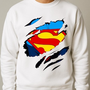 May include: White sweatshirt featuring a Superman logo design. The logo is in the shape of the letter "S" in yellow and red, with blue accents. The design gives the impression of a ripped shirt revealing the logo.
