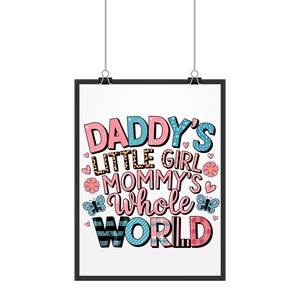 以下が含まれることがあります： ピンク、ブルー、ブラックの文字で「Daddy's Little Girl Mommy's Whole World」と書かれた、黒い額縁のプリント。ハート、蝶、花のパターンが背景になっている。