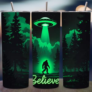 May include: A tall, stainless steel tumbler with a green and black design. The design features a UFO beaming a green light onto a forest with a silhouette of Bigfoot. The word "Believe" is written in green neon font.