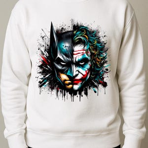 May include: White sweatshirt featuring a split graphic of Batman and the Joker. The Batman side is in dark blue and black, while the Joker side is in green, red, and white. The design has a splatter effect.