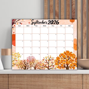Puede incluir: Un calendario de septiembre de 2026 con temática otoñal. El calendario presenta un fondo melocotón con árboles naranjas y amarillos en la parte inferior. Los días de la semana están listados en la parte superior.