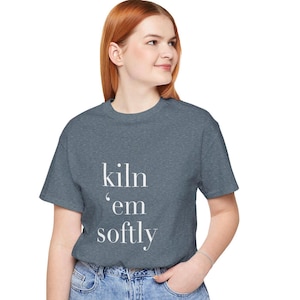 Peut inclure: Un t-shirt gris chiné avec le texte "kiln 'em softly" imprimé en blanc.