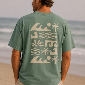 May include: A sage green short-sleeve t-shirt featuring a cream-colored graphic print on the back. The design consists of a grid of stylized beach elements including ocean waves, palm trees, suns, and horizontal lines in a repeating pattern.