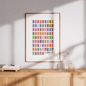 May include: A framed art print featuring a grid of colorful rectangles, each with a unique illustration. The print is titled "THE WRONG LINE" and is displayed on a wooden cabinet. A vase with dried flowers and a small glass bottle are also on the cabinet.
