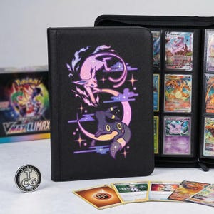 Peut inclure: Classeur de cartes noir avec un motif violet et rose de deux créatures stylisées sur un croissant de lune. Le classeur est ouvert, révélant des pochettes remplies de cartes à collectionner. Une pièce et plusieurs cartes à collectionner sont au premier plan.