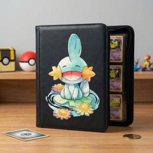 Op de afbeelding: Zwarte binder met een kleurrijke illustratie van een stripfiguur. De binder is open en toont verschillende ruilkaarten. Een kaart en een munt liggen op het houten oppervlak.
