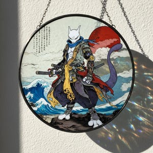 Może przedstawiać: Okrągłe witrażowe dzieło sztuki przedstawiające postać Mewtwo w stylu samuraja. Grafika przedstawia Mewtwo z mieczami, zbroją i powiewającą peleryną, na tle fal oceanu i czerwonego słońca. Element jest oprawiony w czarną metalową ramę i zawieszony na łańcuchu.